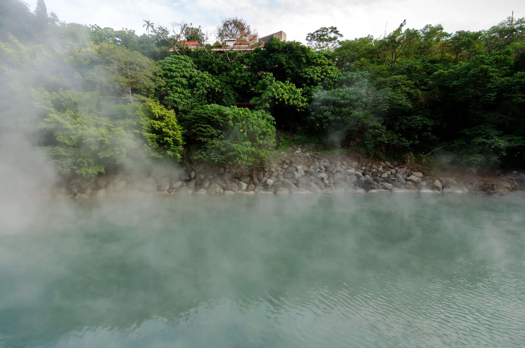 The steaming milky green-blue sulfur hot-spring pool of Beitou Thermal Valley in Taipei, ringed by green hillside