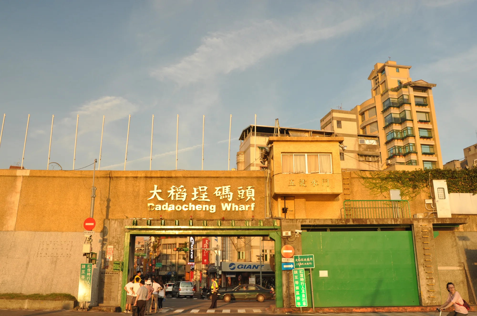 Dadaocheng Wharf in Taipei at golden sunset, with the green riverside floodgate sign reading Dadaocheng Wharf