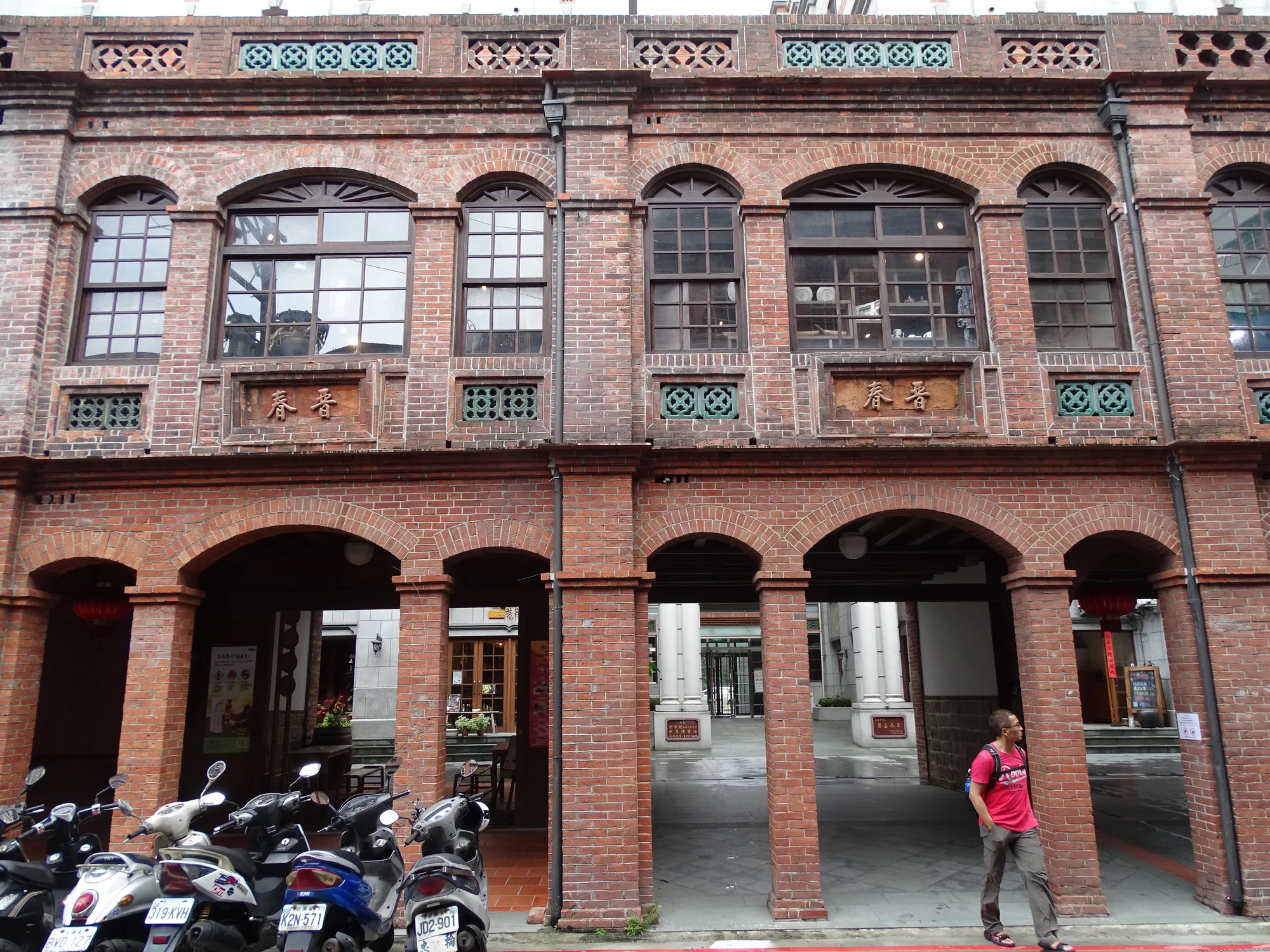A historic red-brick shophouse facade with arched windows and a covered arcade on Dihua Street, Dadaocheng, Taipei