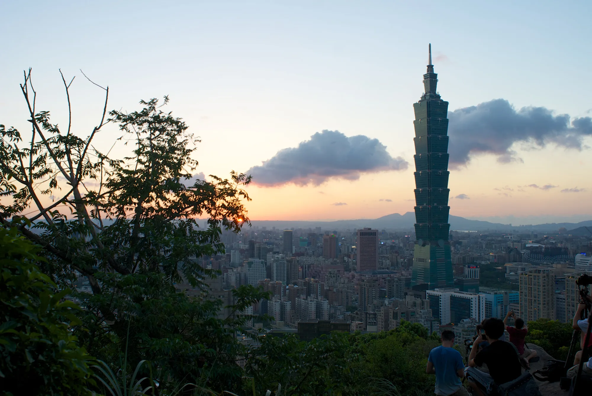 The Elephant Mountain (Xiangshan) trail view at dusk, with Taipei 101 and the city skyline behind dark foreground foliage