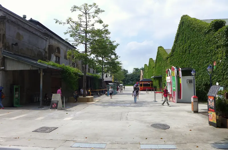 Huashan 1914 Creative Park in Taipei — ivy-covered former-winery warehouse buildings along a tree-lined boulevard with a red sightseeing tram