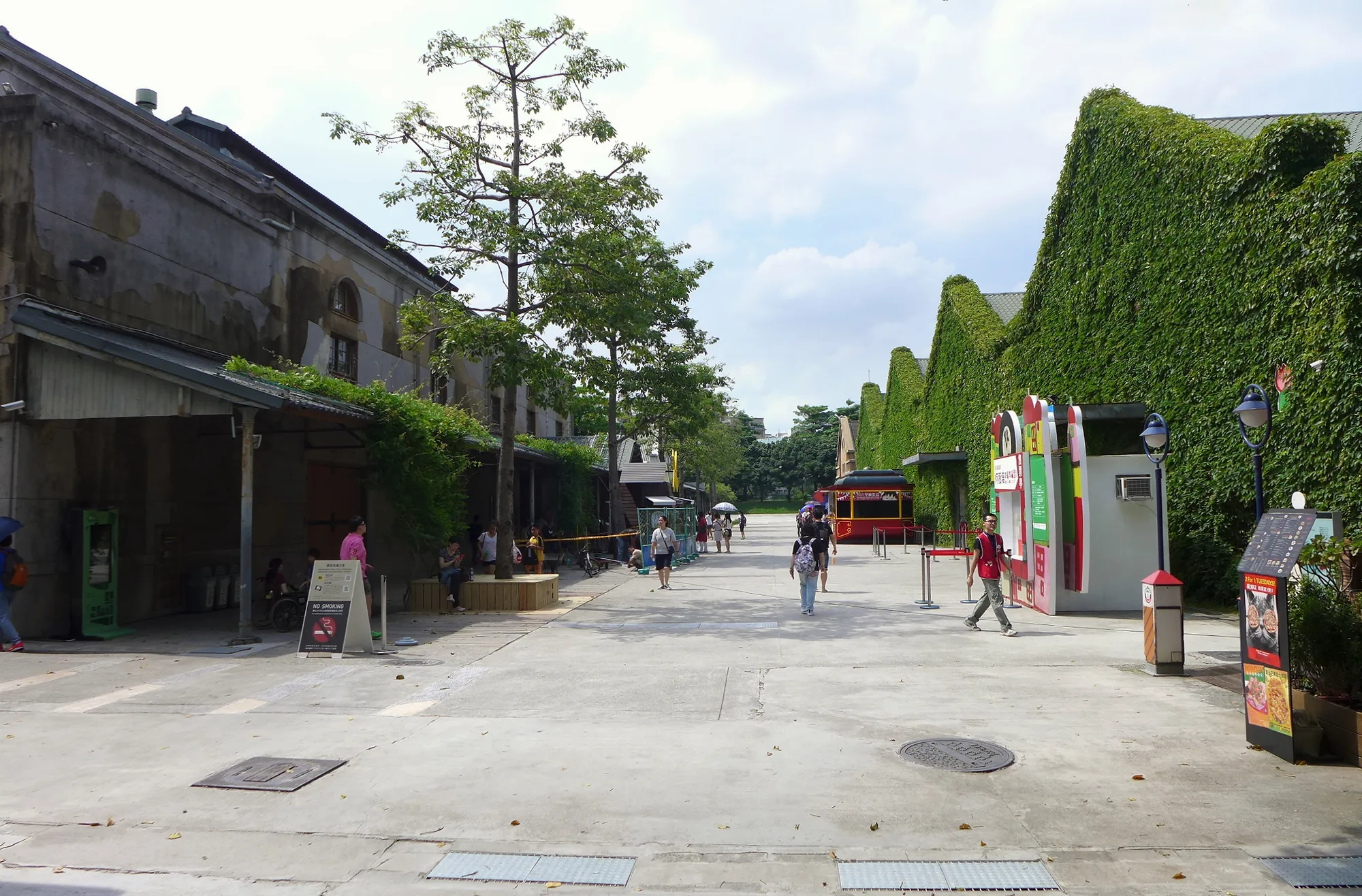 Huashan 1914 Creative Park in Taipei — ivy-covered former-winery warehouse buildings along a tree-lined boulevard with a red sightseeing tram