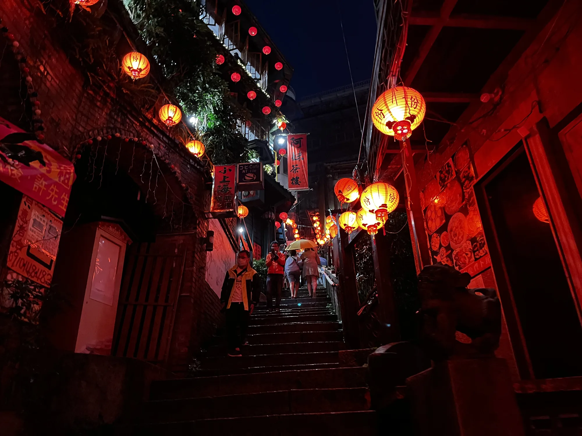The red-lantern stairway of Jiufen old street glowing at night, lanterns lining the narrow alley as people climb the steps