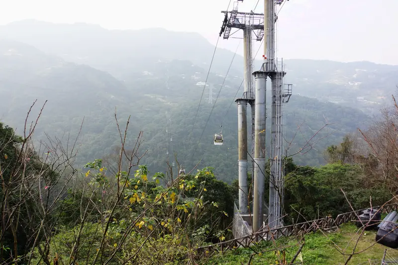 Maokong Gondola cable-car cabins on grey towers descending over forested green tea hills in Taipei