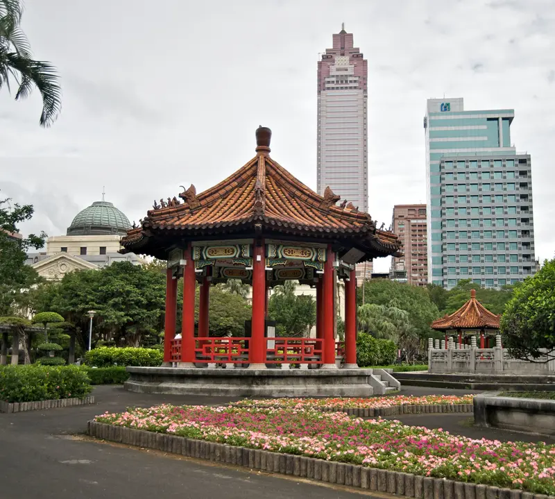 The red-pillared Chinese pavilion at 228 Peace Memorial Park in Taipei, with flower beds and Taipei high-rises behind