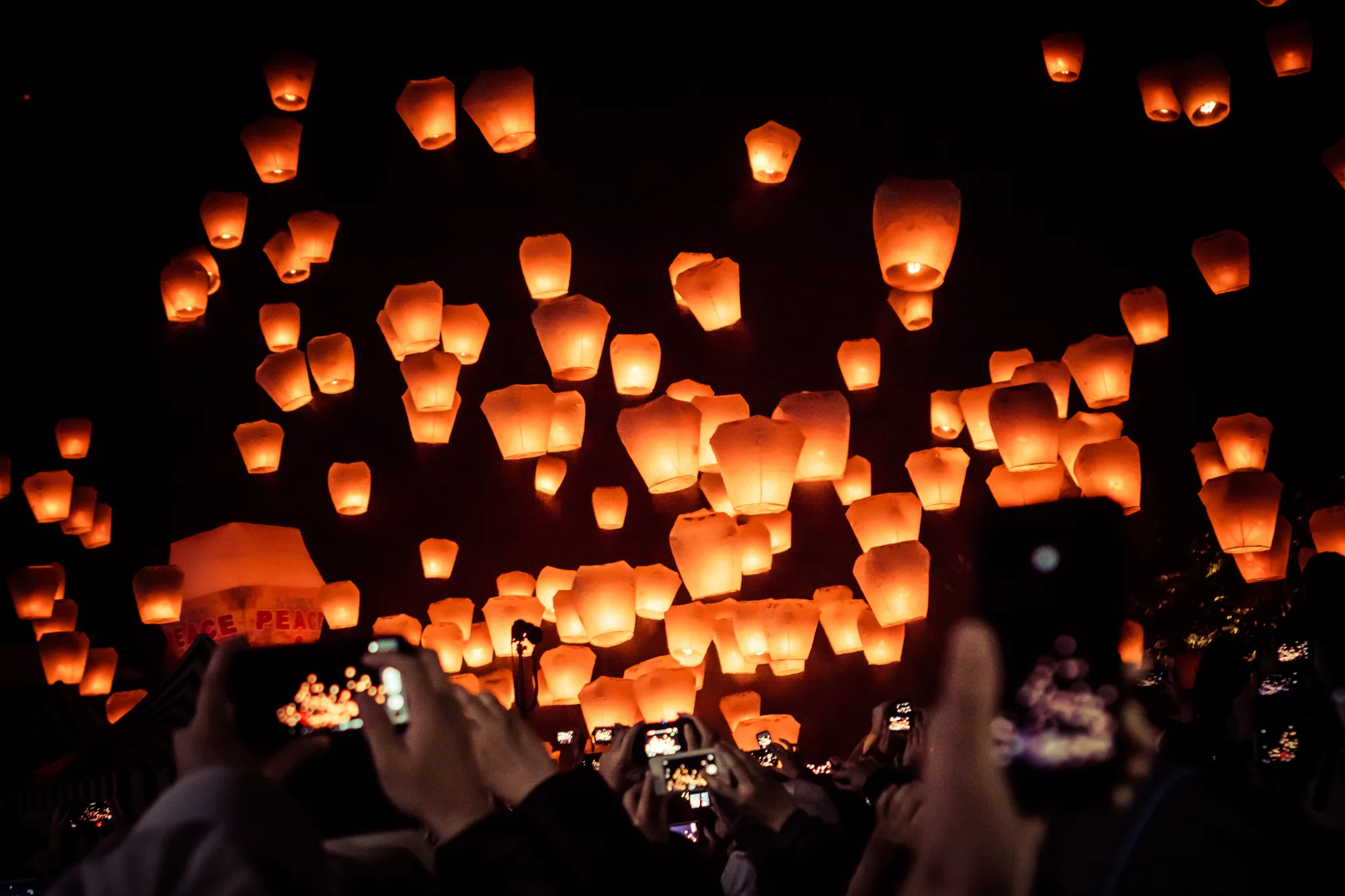 Glowing orange paper sky lanterns rising into the night sky over the crowd at the Pingxi Sky Lantern Festival, Taiwan