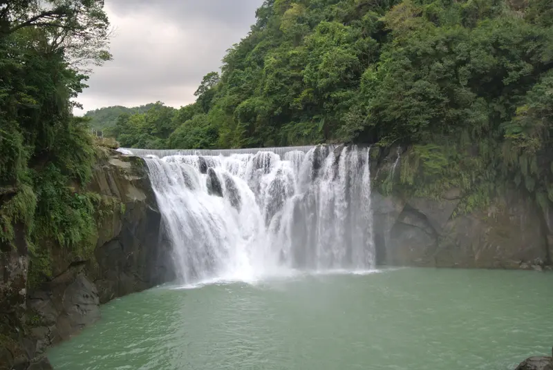 The wide curtain of Shifen Waterfall cascading into a turquoise plunge pool, framed by green forest, in Pingxi, Taiwan