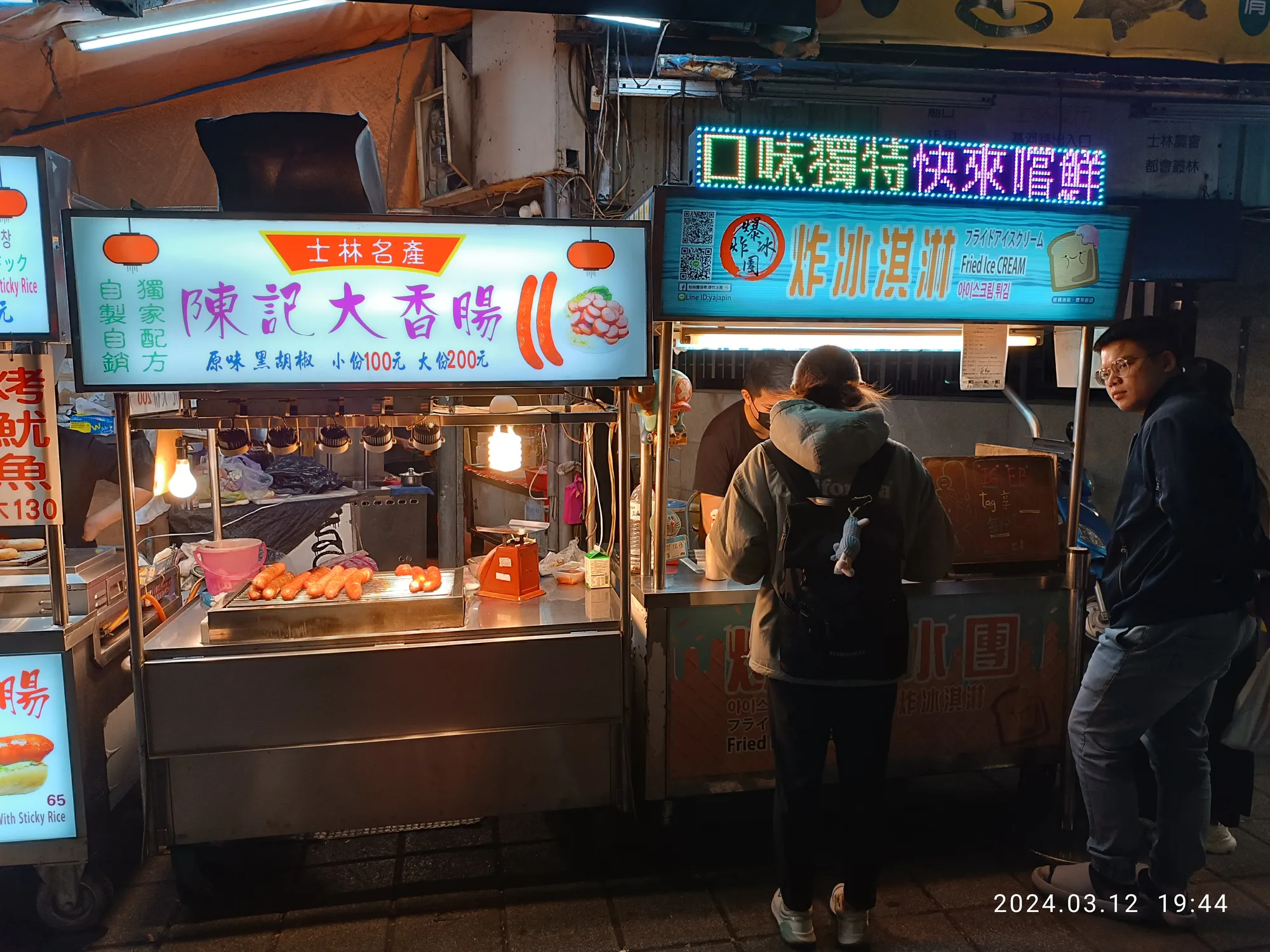 Illuminated food stalls at Shilin Night Market in Taipei at night, with glowing Shilin specialty signs and customers