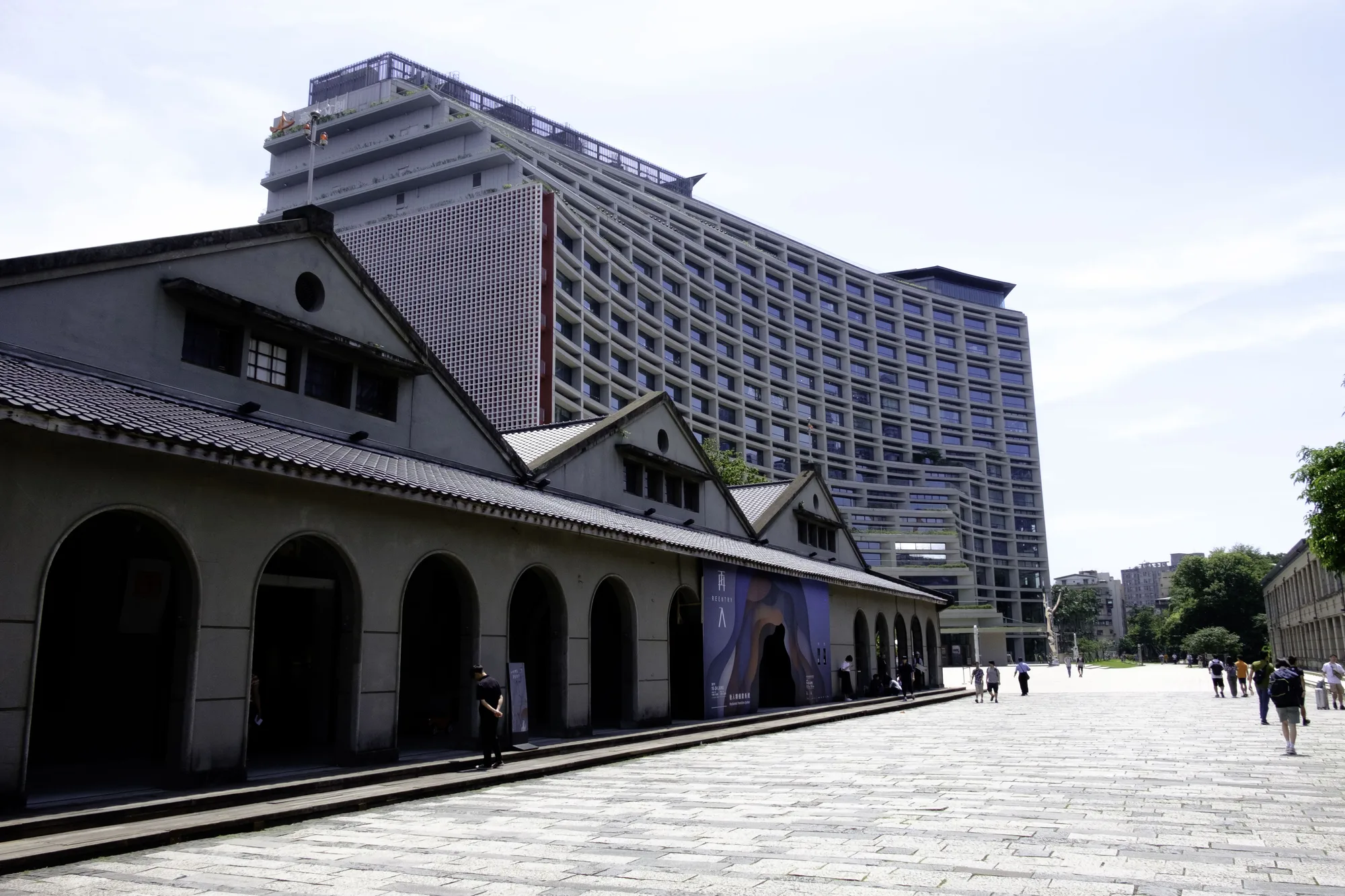 Songshan Cultural and Creative Park in Taipei — the historic tobacco-factory warehouses with the curved Taipei New Horizon building behind