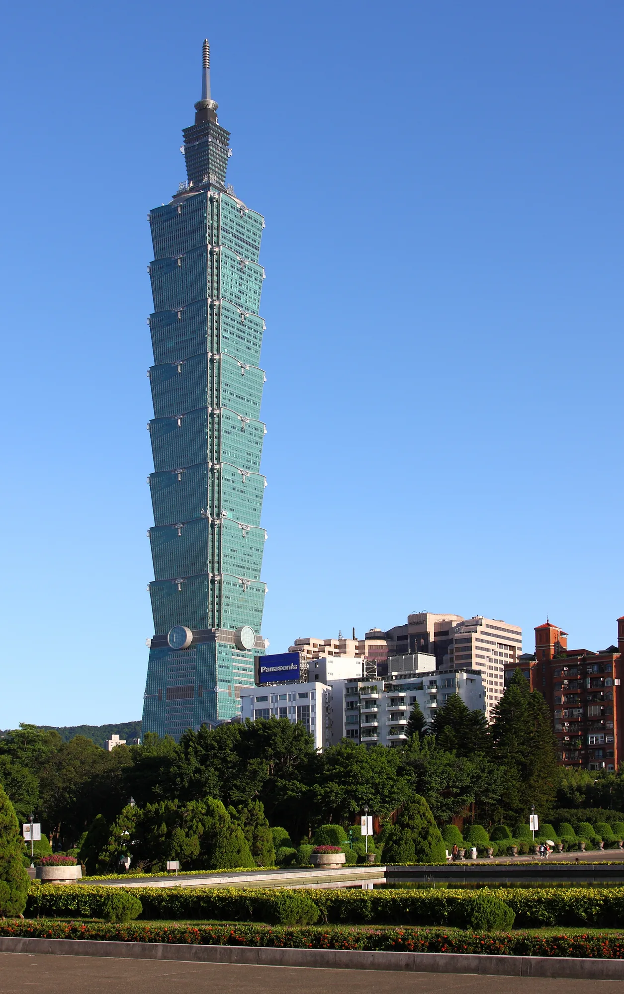 A daytime portrait of the Taipei 101 tower against a clear blue sky, its pagoda-tiered green-glass form clearly visible