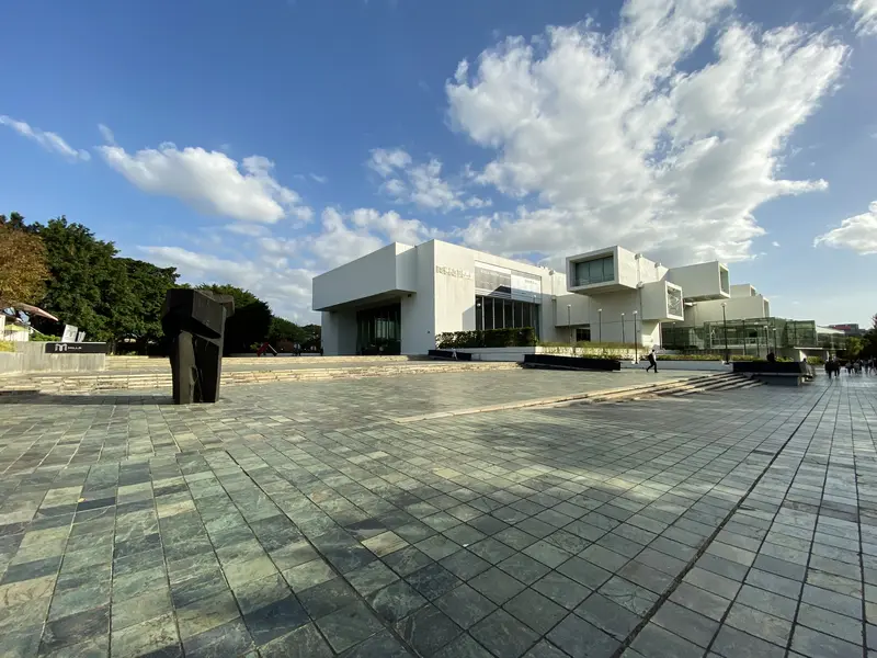 The Taipei Fine Arts Museum (臺北市立美術館) — the white cantilevered modernist building beside its open stone plaza, with an outdoor sculpture and blue sky
