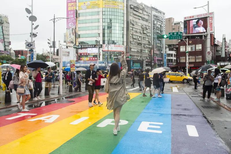 The Ximending rainbow pedestrian crossing in Taipei packed with people, surrounded by neon signage and billboards