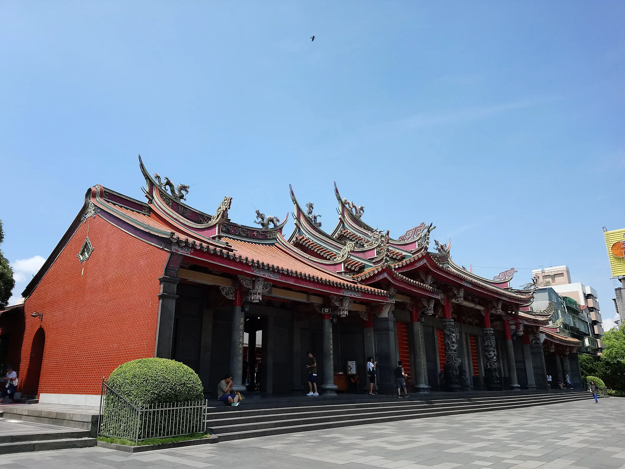 The red-walled Xingtian Temple main hall in Taipei with its ornate swallowtail roof under a blue sky